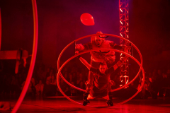 Zwei Personen in roten Kostümen in einem großen Metallreifen; darüber schwebt ein roter Ballon.