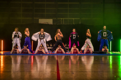 Mehrere Personen in Sportkleidung stehen und liegen auf Matten in einer Turnhalle.