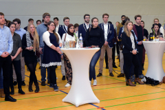 Gruppe von Personen in einer Halle, stehend um Stehtische mit Gläsern und Getränken.