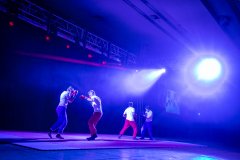 Vier Personen mit Boxhandschuhen auf einer Bühne unter blauem Licht und Nebel.