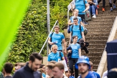 Menschen in blauen Shirts steigen eine lange Außentreppe hinunter, umgeben von dichtem Grün.