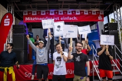 Demonstrierende Menschen mit Protestschildern auf einer Bühne bei einer Veranstaltung der Sparkasse.