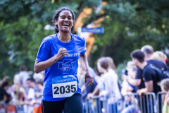 Läuferin in blauem T-Shirt mit Startnummer 2035 läuft auf einer Straße, Zuschauer stehen am Rand.
