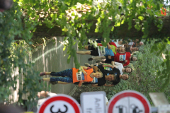 Mehrere Läuferinnen und Läufer auf einem schmalen Waldweg, einige mit Startnummern, von Bäumen und Verkehrsschildern umgeben.
