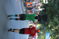 Zwei Läufer auf einer Straße, einer mit grüner, einer mit roter Kleidung; beide halten Stäbe hoch.