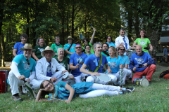 Gruppe von Personen in bunten T-Shirts mit Trommeln und Instrumenten auf einer Wiese im Wald.