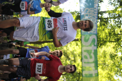 Läufer bei einem Straßenlauf, vorne zwei Männer mit Startnummern 495 und 137 unter einem Startbanner.