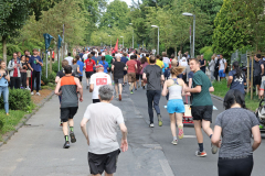 Viele Menschen laufen auf einer breiten Straße, von Bäumen gesäumt, einige mit roten Fahnen.
