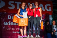 Drei Athletinnen stehen gemeinsam auf dem Siegerpodest und halten Urkunden sowie Geschenktüten.