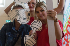 Drei Personen halten einen großen Rahmen; eine hält ein Hantel-Schild, oben steht „#BEACTIVE“.