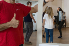 Mann im roten T-Shirt hält einen #BEACTIVE-Rahmen; im Hintergrund stehen mehrere Personen in einem Raum.