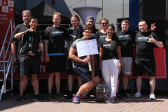 Gruppe von zehn Personen vor einer Bühne, viele in schwarzen „ENERGIE bewegt“-Shirts; eine Person hält ein Schild „NOWUM-Energy“.