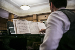 Mann von hinten am Klavier; Notenheft offen, Smartphone links auf dem Klavier.