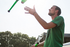 Mann mit grünem T-Shirt jongliert drei grüne Keulen im Freien.