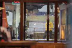 Blick durch Fenster auf eine schneebedeckte Fläche mit zwei Personen, eine in gelber Jacke.
