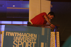 Person in rotem Shirt lehnt über ein Geländer vor einem RWTH Aachen University Sport-Banner.