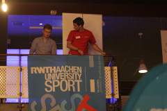 Zwei Männer stehen auf einer Galerie hinter einem blauen Banner mit der Aufschrift „RWTH AACHEN UNIVERSITY SPORT“.