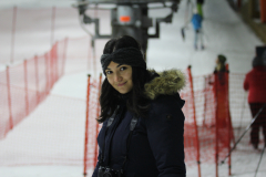 Person mit dunkler Winterjacke und Kamera steht an einer Skipiste mit roten Absperrnetzen.