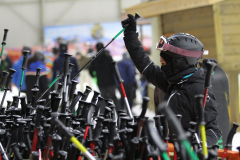 Person mit Helm und Skibrille hält einen Stock; viele Stöcke stehen im Vordergrund.