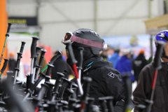 Person mit Helm und Skibrille zwischen mehreren Skistöcken in einer Halle