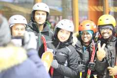 Mehrere Personen in Skihelmen und Winterkleidung halten Skier in die Kamera, eine Hand zeigt ein Friedenszeichen.
