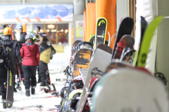 Mehrere Personen in Ski- und Snowboardkleidung stehen in einer Halle neben aufgereihten Snowboards.