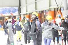 Mehrere Personen mit Ski- und Snowboardausrüstung vor einem Gebäude im Schnee, einige mit Helmen und Skibrillen.