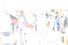 Mehrere Personen mit Helmen und Snowboards in einer verschneiten Halle.