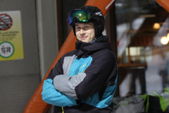 Person mit Skibrille, schwarzer Sturmhaube und blau-grauer Jacke, Arme vor der Brust verschränkt.