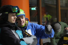 Mehrere Personen in Skikleidung mit Helmen und Handschuhen beugen sich nach vorn im Innenraum.