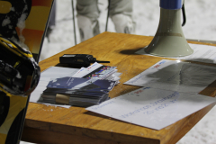 Holztisch mit Stapel von Karten, Funkgerät, mehreren Papieren und einem Megafon; links ein Ski.