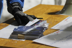 Hand in schwarzem Handschuh neben gestapelten Broschüren auf einem Holztisch.