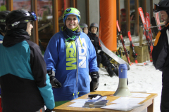 Personen mit Skihelm an einem Tisch mit Megafon und Papier; im Hintergrund Ski und Schnee.