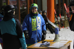 Mehrere Personen in Skihelm und Winterkleidung stehen an einem Tisch mit Megafon und Papieren im Schnee.