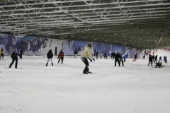 Indoor-Skihalle mit mehreren Personen beim Skifahren und Snowboarden auf einer schneebedeckten Piste.