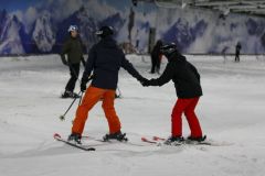 Zwei Skifahrer halten sich beim Üben in einer Skihalle an den Händen.