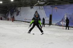 Skifahrer trägt ein Kind auf den Schultern in einer Indoor-Skihalle.