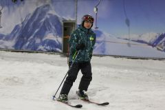 Person beim Skifahren in einer Indoor-Skihalle vor Bergkulisse.
