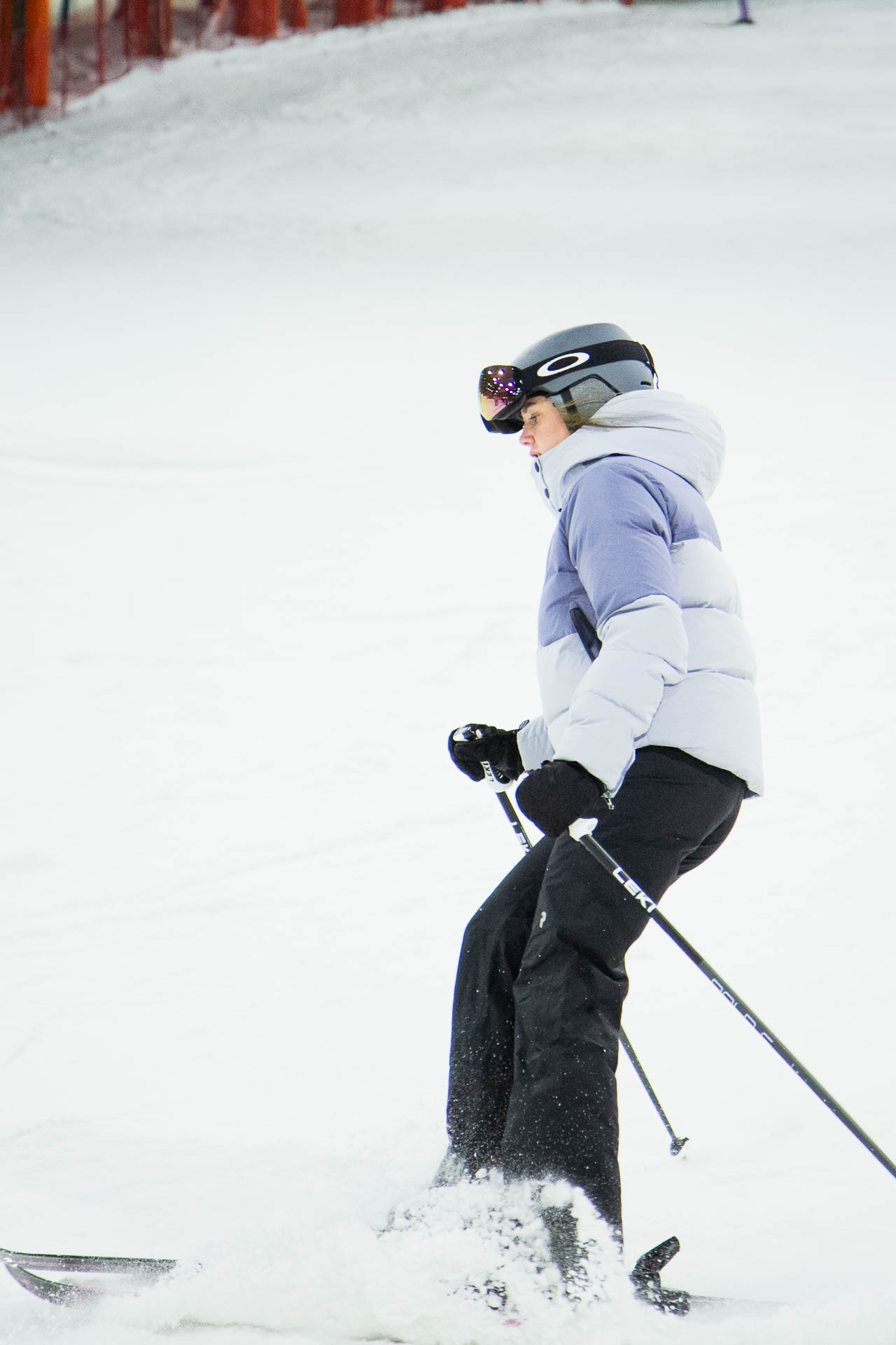 Skifahrer in weißer Jacke und schwarzer Hose bei Winteraktivität, mit Schnee sprühend.