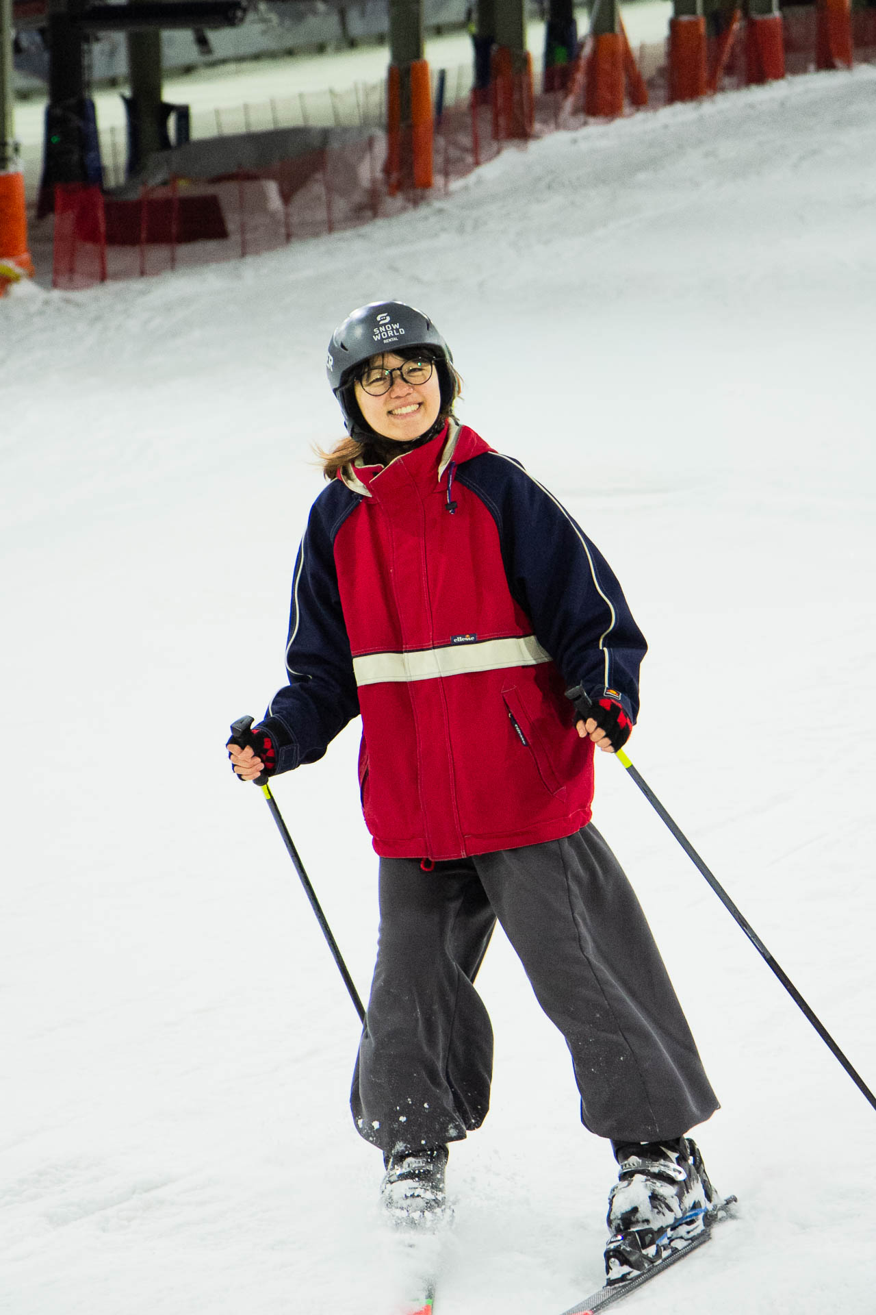 Schneesportler mit schwarzer Jacke, roter Hose und Helm vor Winterhintergrund.