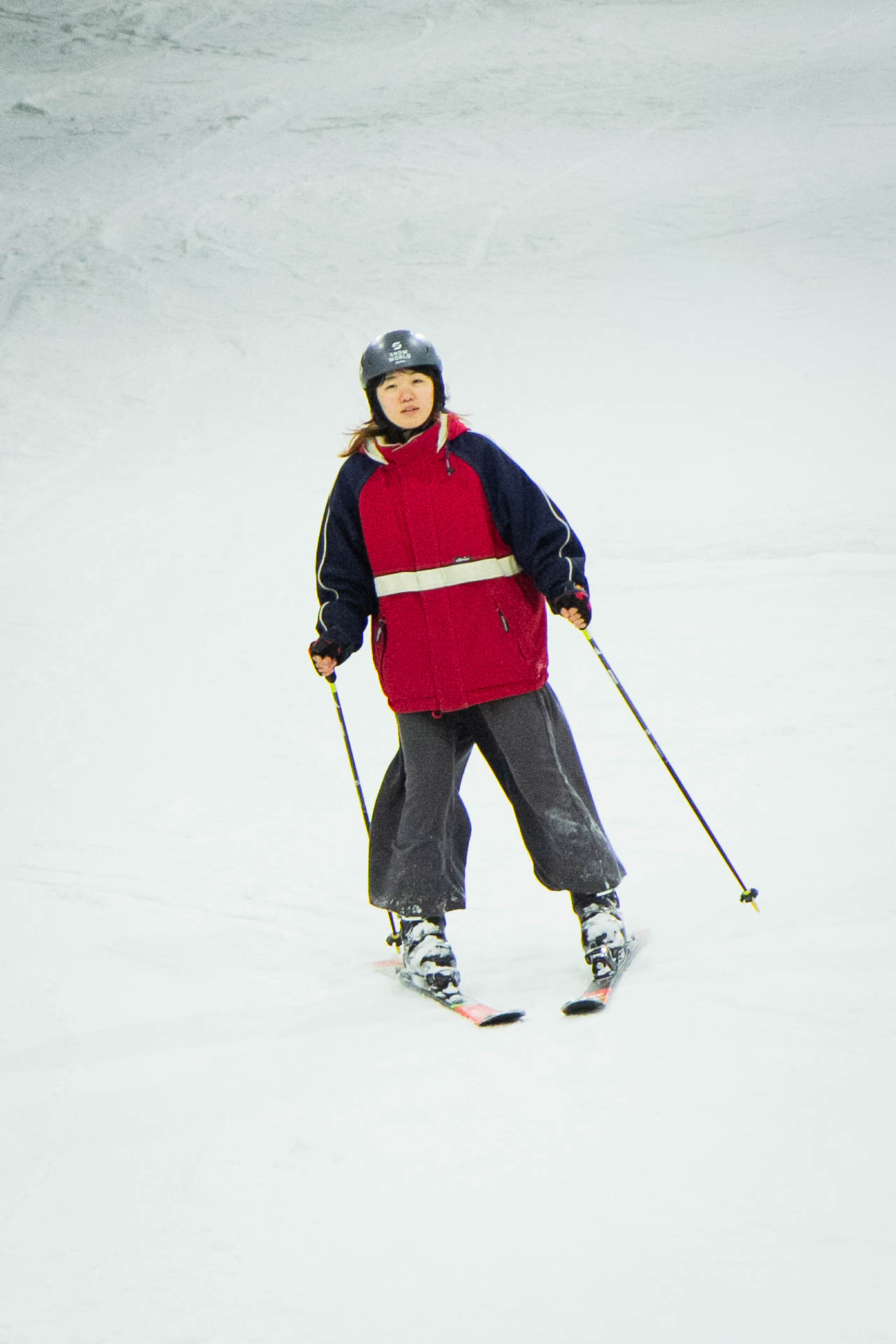 Person in rot-schwarzer Jacke mit Ski und Stöcken auf Schnee.