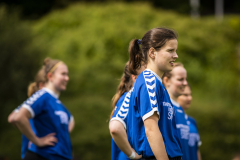 Mehrere Personen in blauen Sporttrikots stehen im Freien, eine im Vordergrund im Profil.