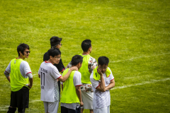 Sechs Männer auf einem Fußballrasen, einige in gelben Westen und weißen Trikots, von hinten und seitlich.