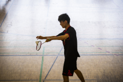 Person beim Badminton in einer Halle, mit Schläger und Federball in der Hand.