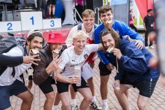 Gruppe junger Sportler posiert vor einem Siegerpodest bei einer Veranstaltung.