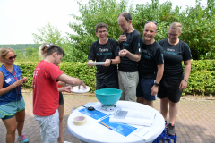 Gruppe von sechs Personen im Freien an einem Tisch mit blauer Schüssel, Papier, Klebeband und Teller.