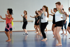 Gruppe von Menschen macht Tanzbewegungen in einem Raum mit Spiegelwand und Ballettstange.