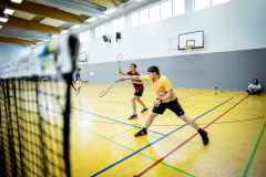 Zwei Männer spielen Badminton in einer Sporthalle.