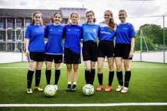 Sechs Fußballspielerinnen in blauen Trikots stehen auf einem Kunstrasenplatz.