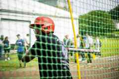 Baseballspieler mit rotem Helm hinter dem Fangnetz auf dem Trainingsfeld.